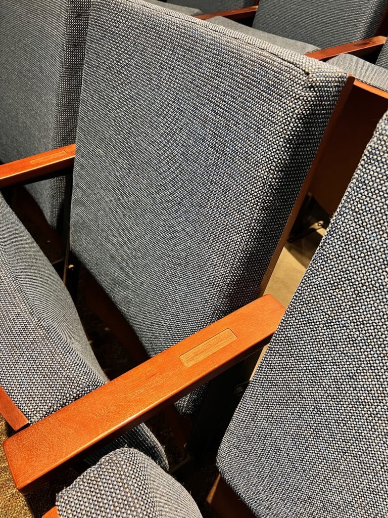Close-up view of empty blue theater seats with wooden armrests.